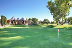 Un campo de golf bien cuidado con un pabellón, árboles y cielo despejado.
