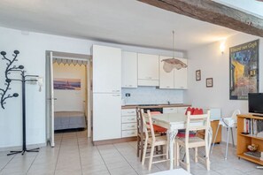 A compact kitchen with white cabinets, a dining table with chairs, and a television on a wooden stand.