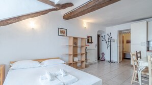 Ein Schlafzimmer mit einem Bett, einer hölzernen Bank, einem kleinen Tisch, einer Heizung und einer Tür zu einem anderen Raum.