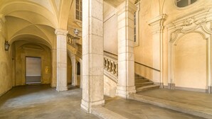 Ein prachtvoller Saal mit Säulen aus Stein, einer Treppe und einer Tür am Ende.