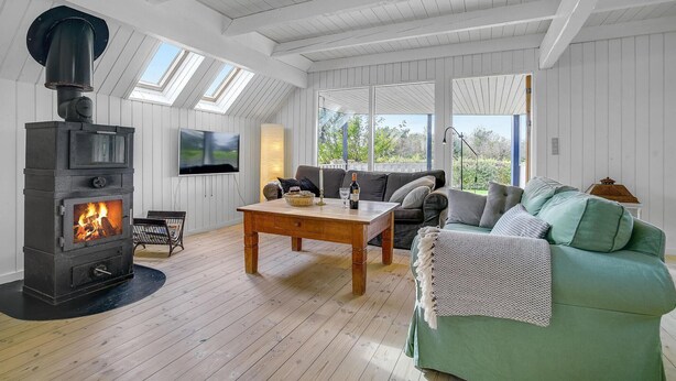 A cozy living room with a wood-burning stove, a television, a sofa, and a table with a candle and glasses. - 3 bedroom lovely home in Slagelse (Slagelse)