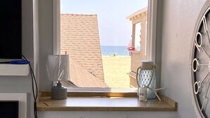 A room with a large window overlooking a beach, a small table with a candle and starfish decoration, and a door with a white frame. - *Immaculate Villa! Waking Distance To All Local Favorites! Steps to the Beach!* (Newport Beach)