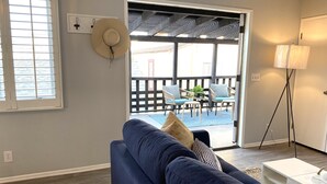 A living room with a blue sofa, a hat on the wall, and a view of an outdoor patio with chairs and a table. - *Immaculate Villa! Waking Distance To All Local Favorites! Steps to the Beach!* (Newport Beach)