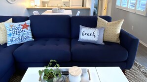 A living room with a dark blue sofa, a white coffee table, and decorative pillows. - *Immaculate Villa! Waking Distance To All Local Favorites! Steps to the Beach!* (Newport Beach)