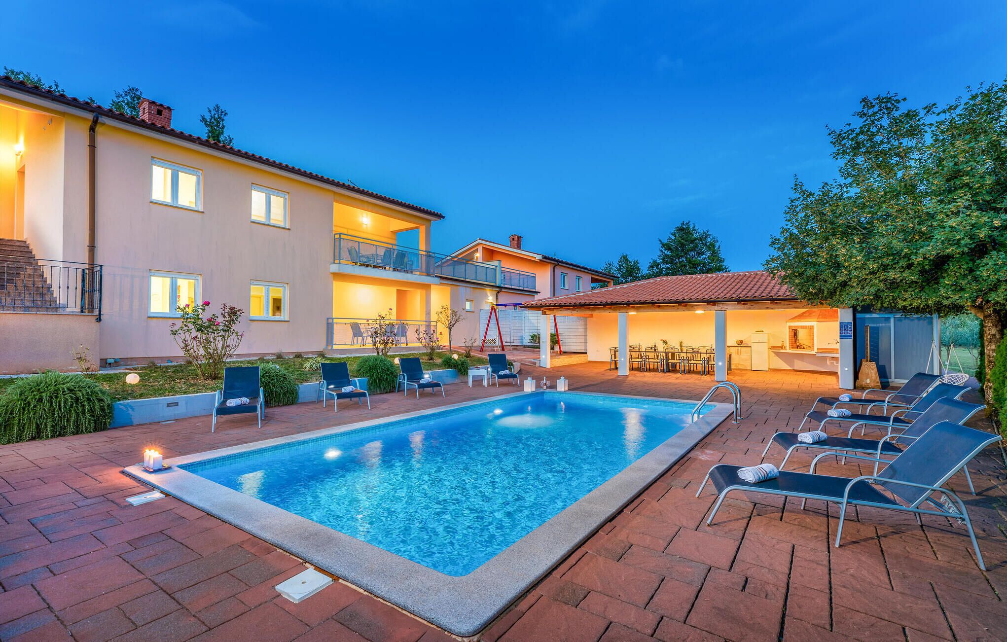 A swimming pool with lounge chairs, a covered patio, and a two-story building with balconies.