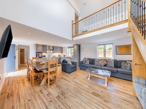 A spacious living area with a dining table, sofas, and a staircase leading to an upper level.