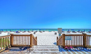 Une terrasse en bois qui mène à une plage agrémentée de parasols et de chaises longues.