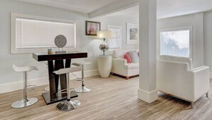 Una sala de estar moderna con comedor, que incluye una mesa de comedor de madera, taburetes de bar, un sofá blanco y una lámpara de pie.