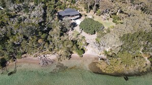 An aerial view of a secluded house surrounded by dense forest and a body of water.