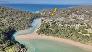 An aerial view of a coastal area with a winding river, a beach, and a dense forest.