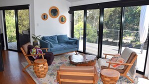 A modern living room with a blue sofa, wooden chairs, a coffee table, and a large sliding glass door leading to a balcony.