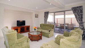 A living room with green sofas, a wooden coffee table, and a TV on a cabinet. - Brand New Home on Perth Doorstep (Bayswater)