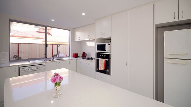 A modern kitchen with white cabinets, a central island, a microwave, an oven, and a refrigerator. - Brand New Home on Perth Doorstep (Bayswater)