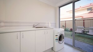 A modern kitchen with a built-in washing machine, a sink, and a sliding glass door leading to a patio. - Brand New Home on Perth Doorstep (Bayswater)