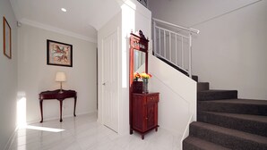 A hallway with a staircase, a wooden cabinet with a mirror, a vase of flowers, and a framed picture on the wall. - Brand New Home on Perth Doorstep (Bayswater)