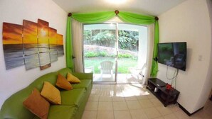 Una sala de estar con un sofá verde, un televisor de pantalla plana y un ventanal corredero que da a un patio.