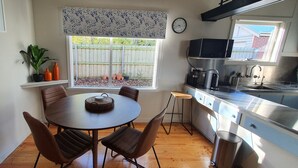 A compact kitchen with a dining area, wooden flooring, and a window with a view of a backyard. - Cosy Mid-Century home, Central, Off Street Parking and Fur Baby Friendly (Newington)