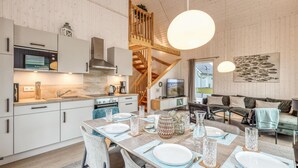 A modern kitchen with white cabinets, a Bosch microwave, and a wooden staircase leading to a loft.