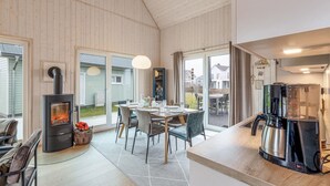 A modern kitchen with a wood-burning stove, a dining area with chairs and a table, and a view of the outside.