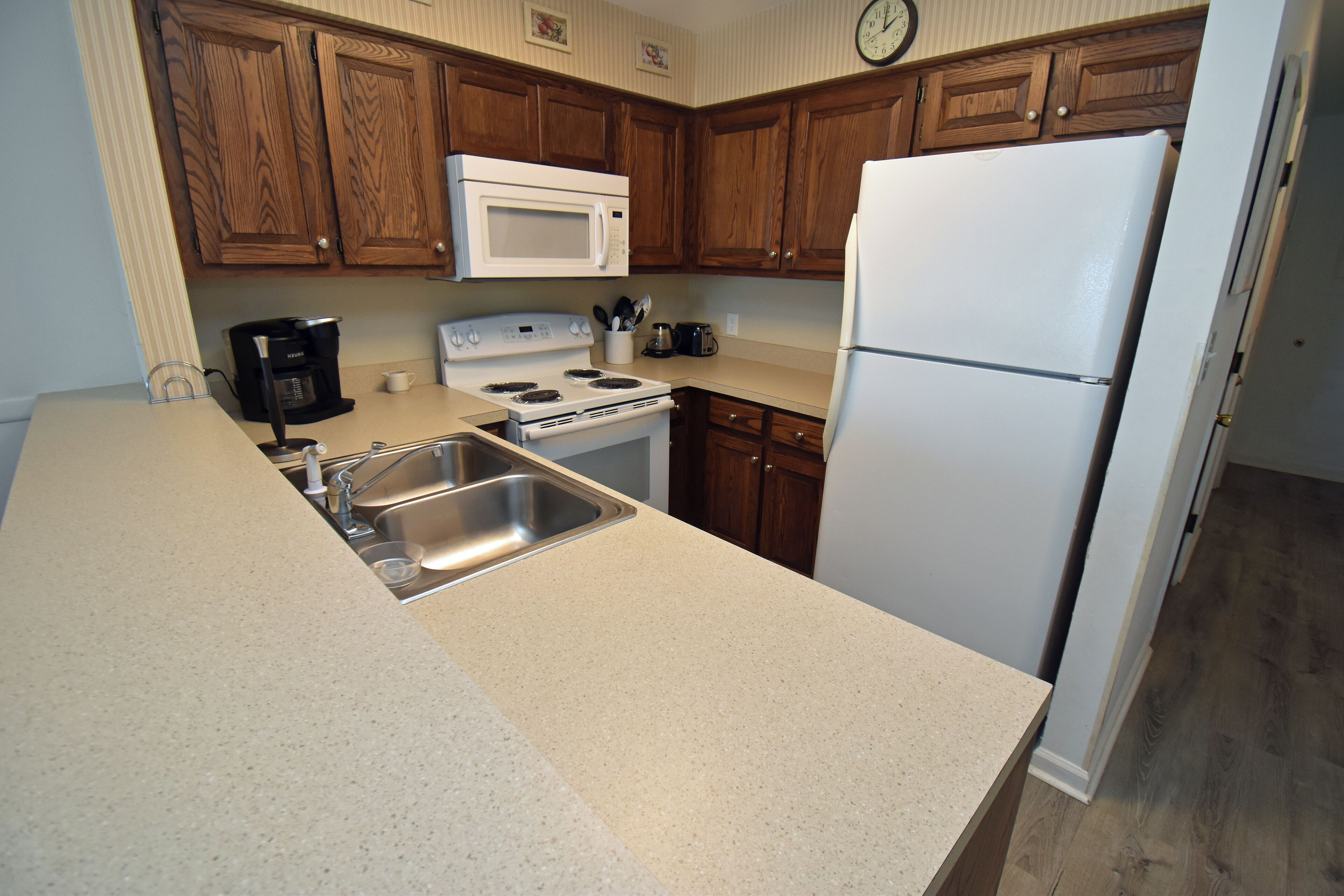 A kitchen with wooden cabinets, a white microwave, a stove, a sink, and a refrigerator.