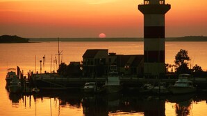 Un phare au coucher du soleil, avec des bateaux amarrés dans une marina.