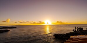 A sunset over a calm sea with a rocky outcrop and a row of chairs facing the water. - Umi No Terrace Yomitan Toya (Yomitan)