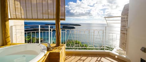 A balcony with a view of the sea, a bathtub, and a wooden deck.