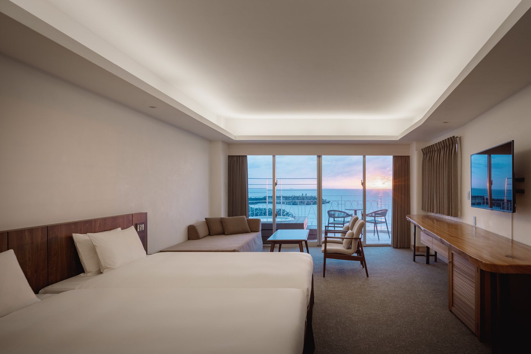 A hotel room with a large bed, a sofa, a small table, a TV, and a balcony with a view.