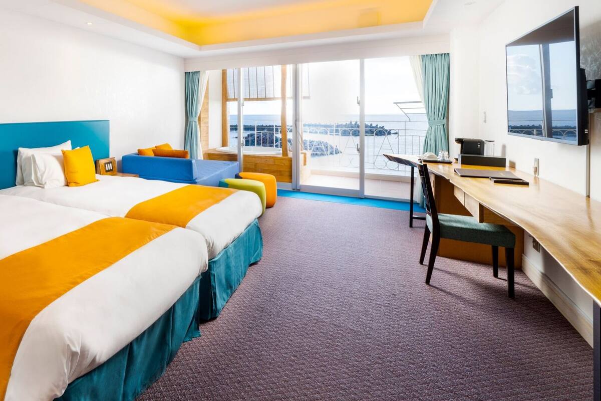 A hotel room with two beds, a desk, and a TV.
