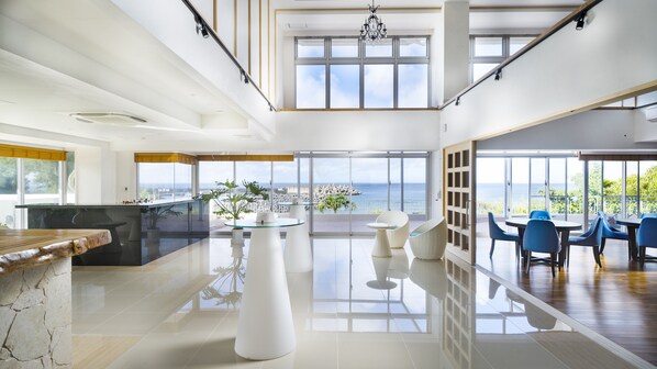 A spacious, modern interior with a large open kitchen, dining area with blue chairs, and a view of the sea through large windows. - Umi No Terrace Yomitan Toya (Yomitan)