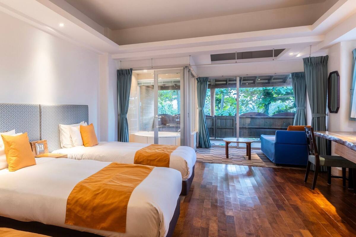 A hotel room with two beds, a desk, and a view of the outdoors.