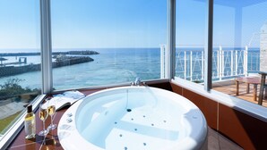 A bathroom with a large bathtub, a window with a view of the sea, and a table with a bottle and glasses. - Umi No Terrace Yomitan Toya (Yomitan)