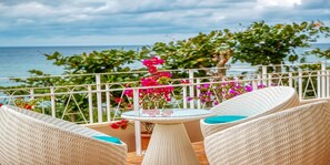 A balcony with wicker chairs and a glass table, overlooking the sea and featuring pink flowers. - Umi No Terrace Yomitan Toya (Yomitan)