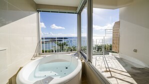 A bathroom with a large bathtub, a view of the sea through a balcony, and a tiled floor. - Umi No Terrace Yomitan Toya (Yomitan)