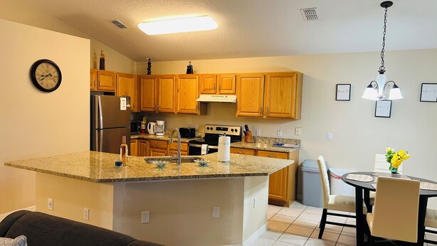 Una cocina moderna con armarios de madera, encimeras de granito, electrodomésticos de acero inoxidable y una zona de comedor con una mesa y sillas.