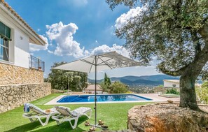 Une piscine entourée de murs de pierre et de verdure, avec des chaises longues et un parasol.