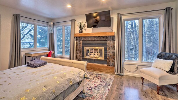 A bedroom with a bed, a chair, a fireplace, and large windows. - Water-View Retreat By Coastal Trail & Downtown! (Anchorage)