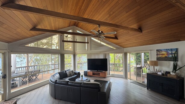 A spacious living room with a large sectional sofa, a flat-screen TV, and a ceiling fan. - The Lake House on Amaroo Waterfront/Free WiFi/Includes Linen, SUP Boards/Kayaks  (Smiths Lake)
