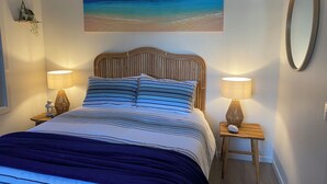 A bedroom with a bed, two bedside tables with lamps, a wall-mounted mirror, and a painting of a beach scene. - The Lake House on Amaroo Waterfront/Free WiFi/Includes Linen, SUP Boards/Kayaks  (Smiths Lake)