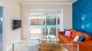 A modern living room with a glass coffee table, a sofa with colorful cushions, and a TV mounted on the wall.