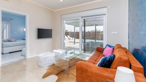A modern living room with a glass coffee table, an orange sofa, and a TV mounted on the wall.