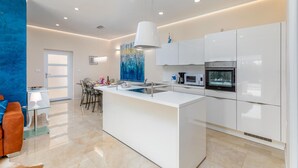 A modern kitchen with white cabinets, a central island, stainless steel appliances, and a blue abstract painting on the wall.