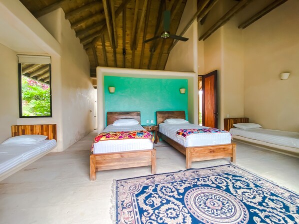 Une pièce avec deux lits en bois, un grand tapis bleu à motifs et un ventilateur de plafond.