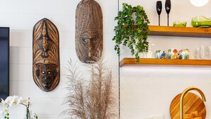 A modern kitchen with a wooden countertop, a green chair, and decorative masks on the wall. - Muse- Luxe Apartment in Port Douglas (Port Douglas)