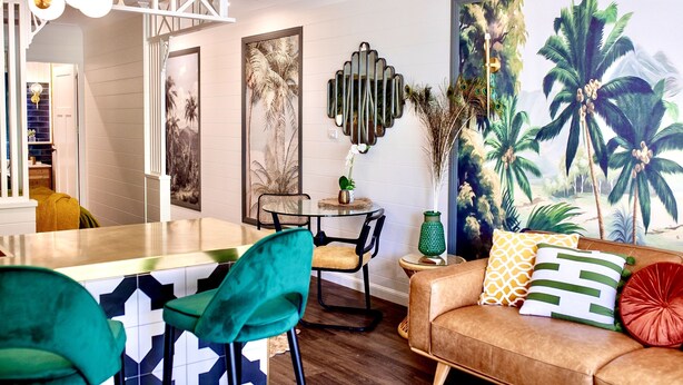 A modern living room with a dining area, featuring a large tropical mural, a round table, and a sofa with decorative pillows. - Muse- Luxe Apartment in Port Douglas (Port Douglas)