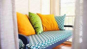 A sofa with patterned cushions and a blue frame, positioned in a room with white blinds.