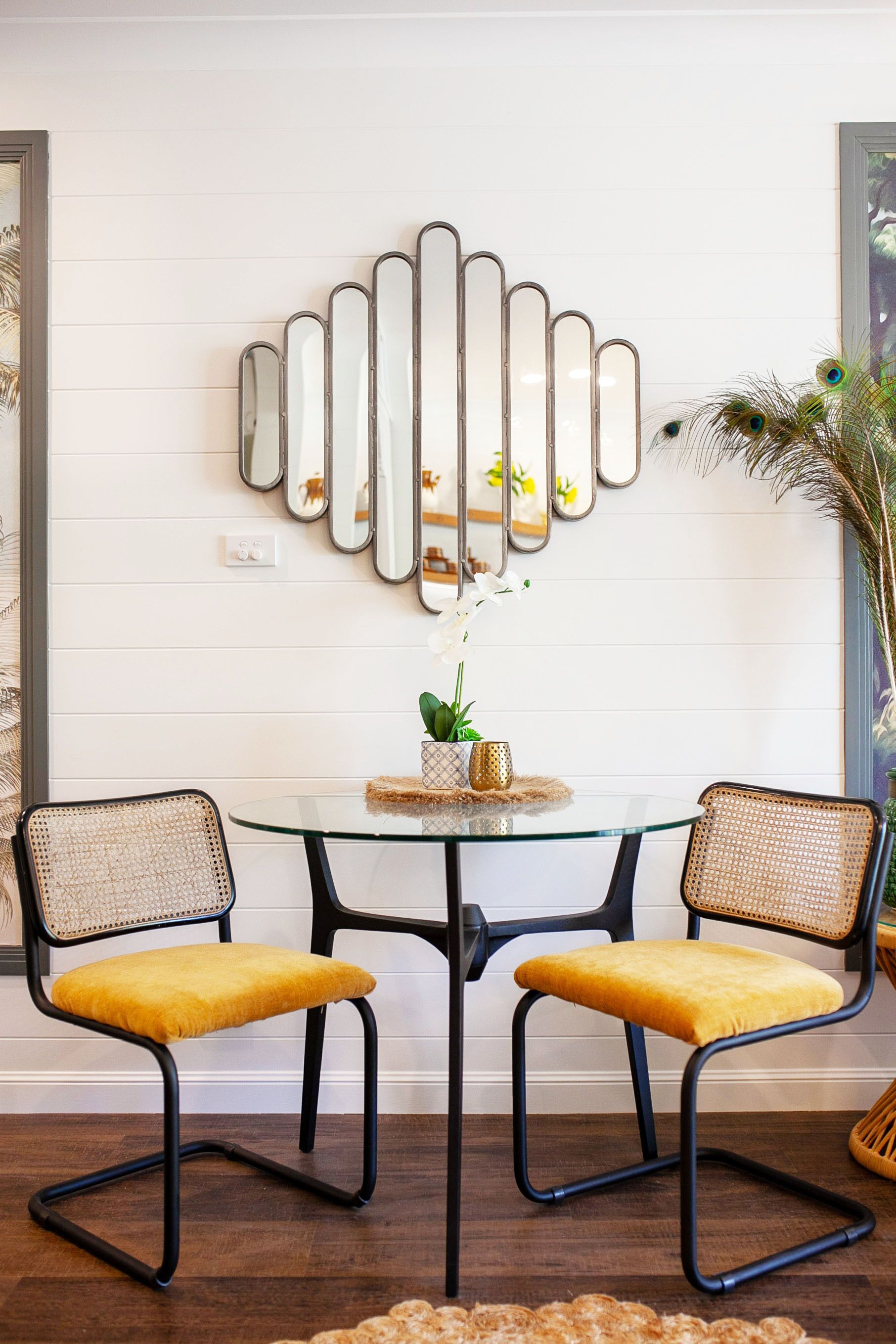 A dining area with two chairs, a glass table, and a wall-mounted mirror.