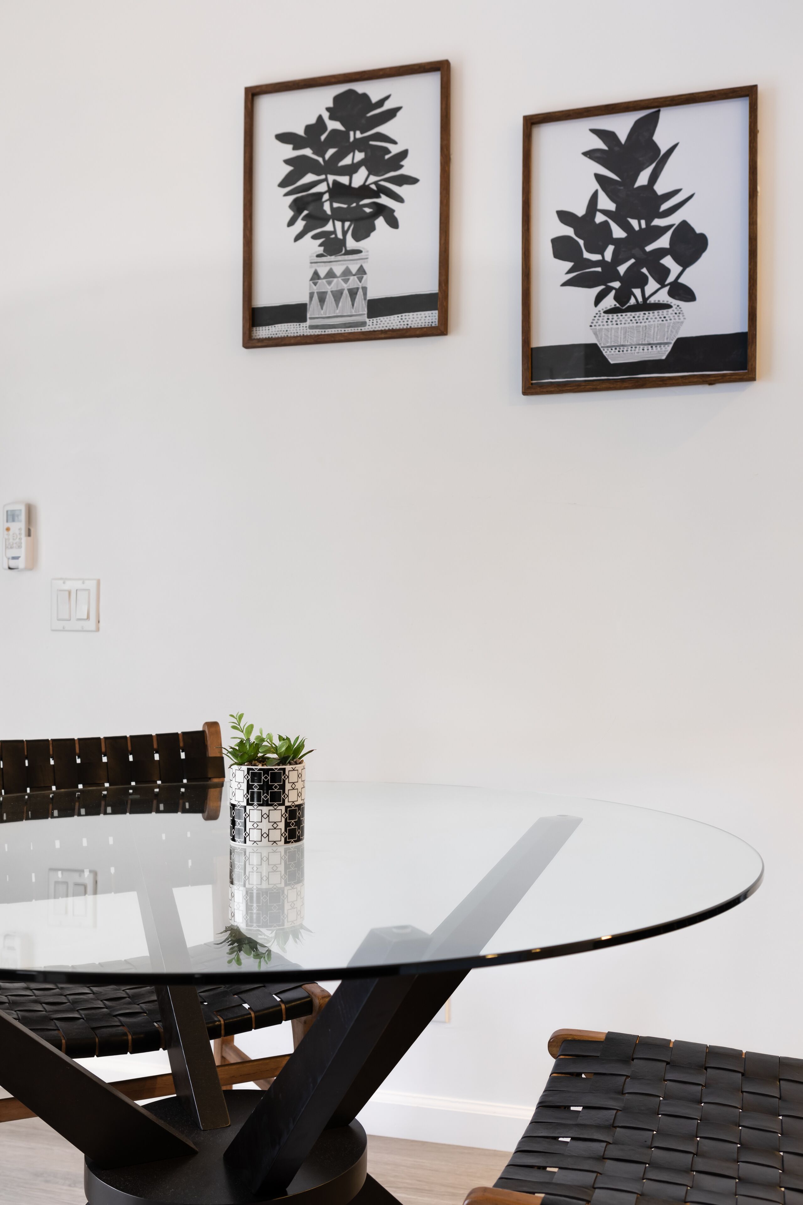 Un comedor moderno con una mesa de vidrio, dos sillas y una planta en maceta sobre la mesa.