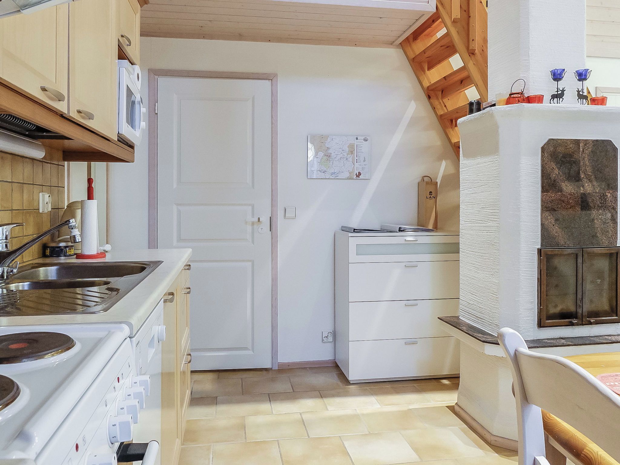 Een kleine keuken met een kookplaat, gootsteen en kastjes, een deur naar een andere kamer, en een kleine koelkast.
