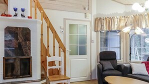 Una sala de estar acogedora con chimenea, una escalera de madera, un sofá y una mesa.